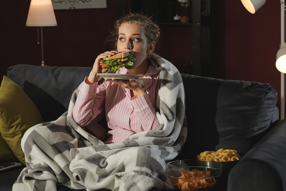 young woman eating a sandwich and snacks late at night