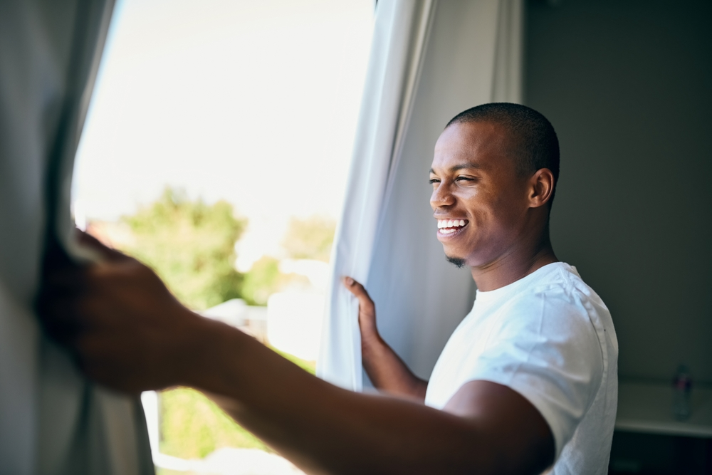 smiling man opening curtains to let in sunlight