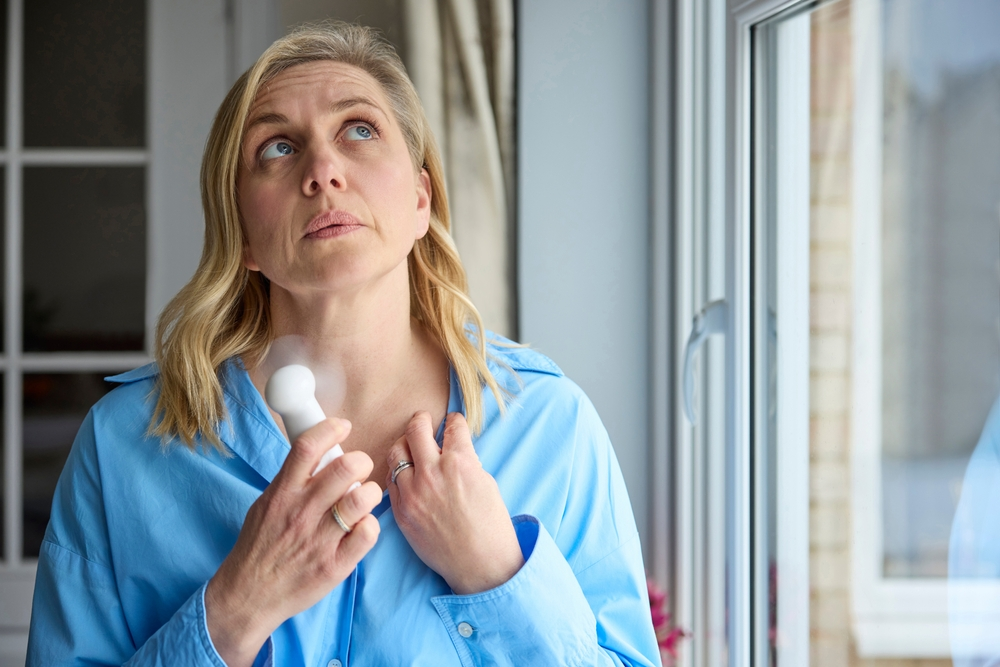 woman holding portable fan to cool off during hot flash