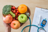 heart-shaped bowl of fruits and vegetables next to stethoscope and blood sugar test device