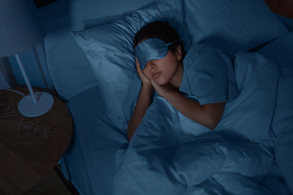 woman sleeping in bed in dark room wearing eye mask