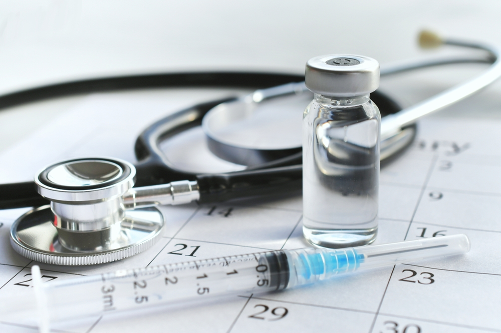 vaccine vial, syringe, and stethoscope on calendar