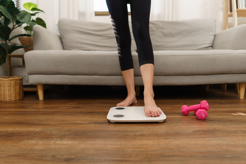 woman stepping on floor scale next to dumbells