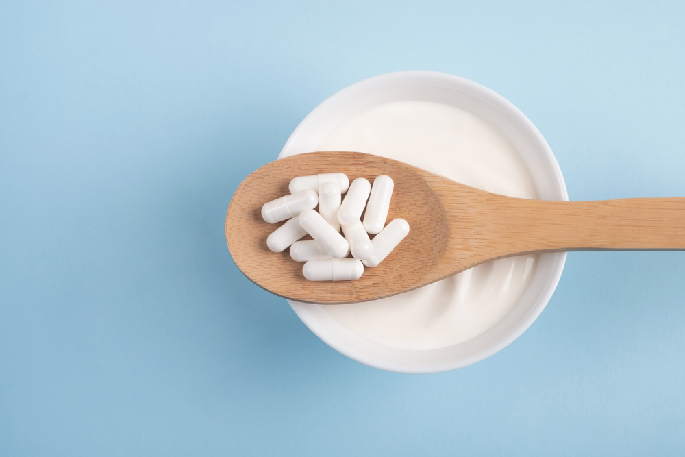 probiotic capsules on wooden spoon over cup of yogurt